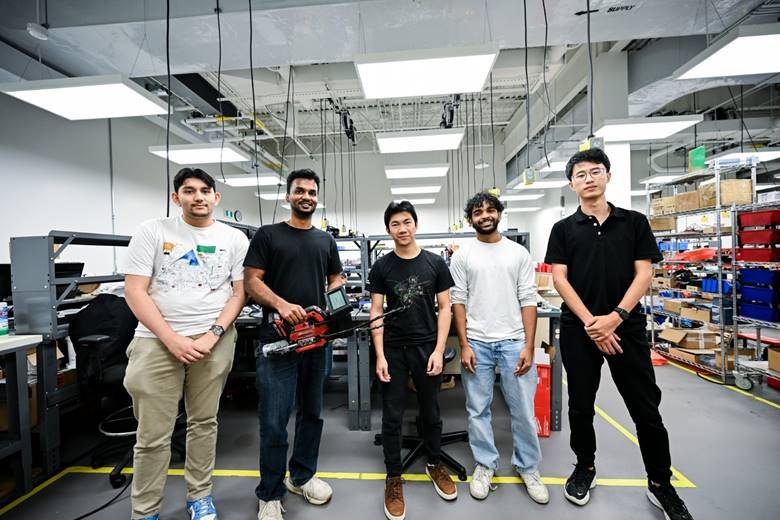 Five members of the GreaseTech team standing in their lab, one holding the smart grease gun with its screen mounted on top.